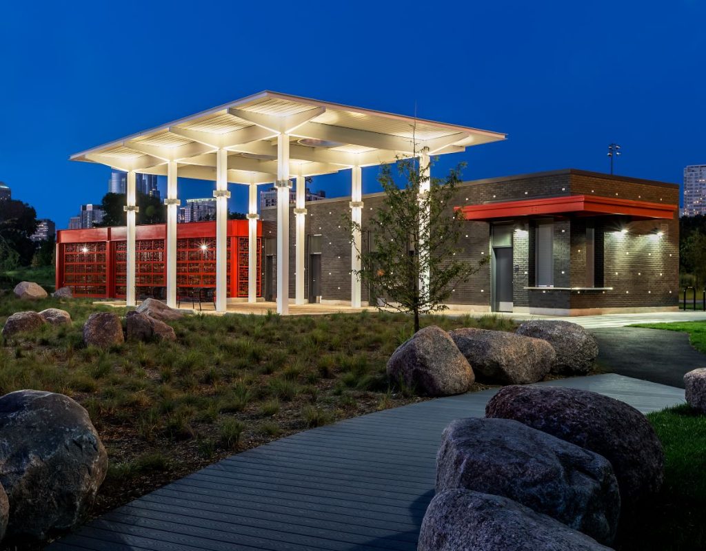 The stylish Ping Tom Boathouse is a brown building with bright red highlights. A lit white canopy stands in front.