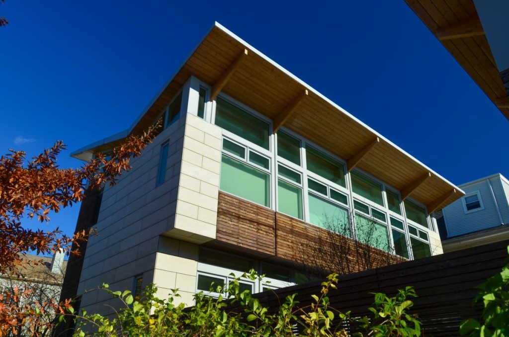 A street level view of a "green" residence on Chicago's North Side shows a unique slanted roof for gathering rainwater. Large windows with light green drapes cover the upper story on the back of the house. 