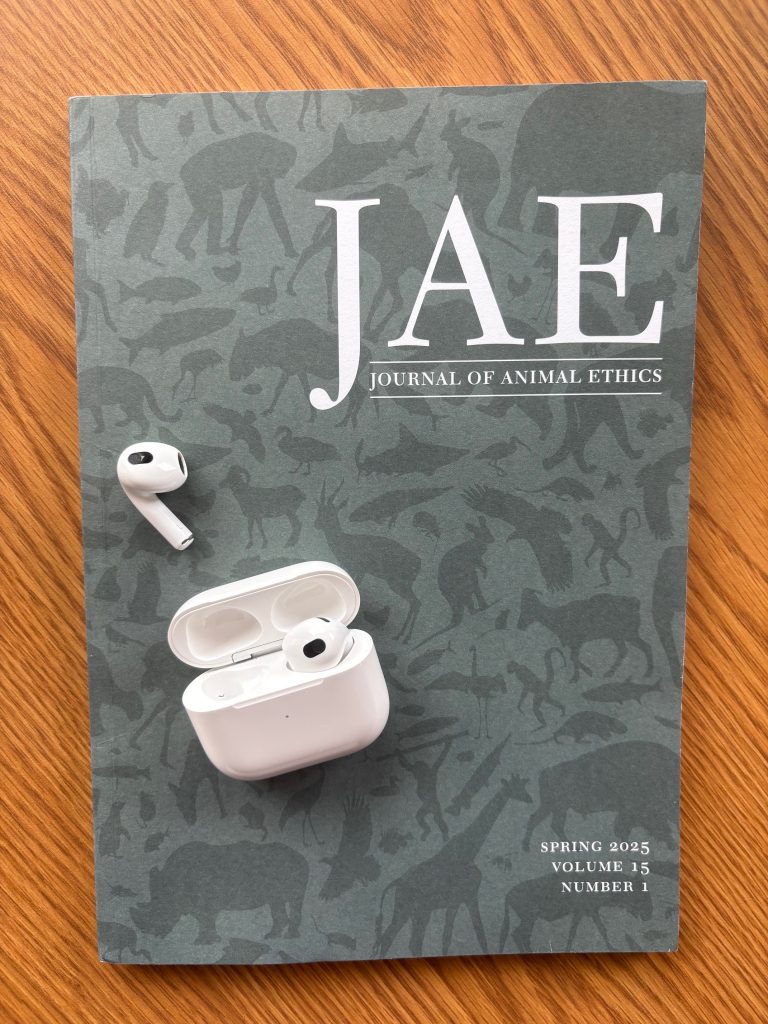 Issue of Journal of Animal Ethics on a wooden table, with an open headphone case to indicate listening to a podcast