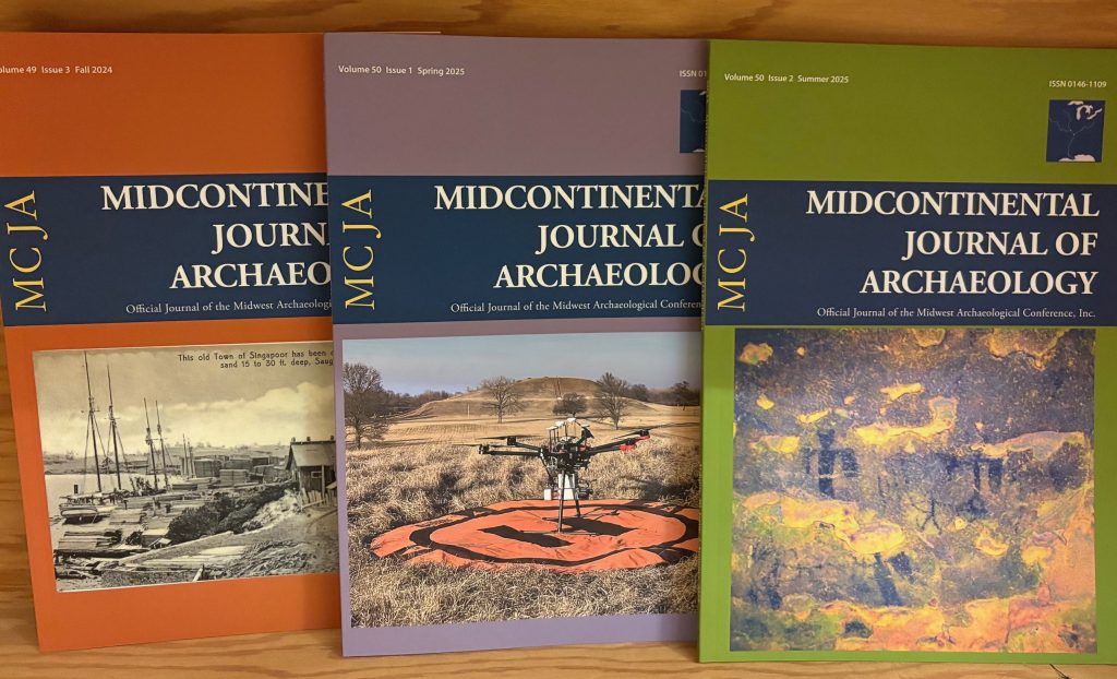 Three issues of Midcontinental Journal of Archaeology on a wooden shelf.