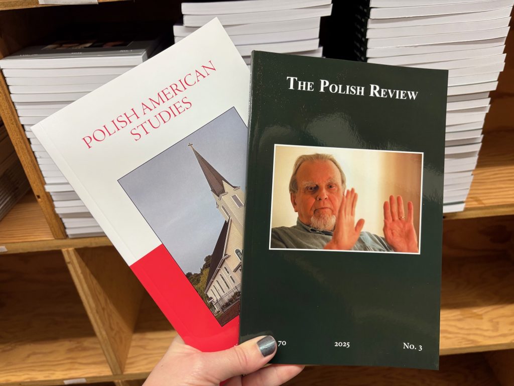 Copy of Polish American Studies Vol. 82, Iss. 1, and The Polish Review Vol. 70, Iss. 3 held in front of a shelf of journals.