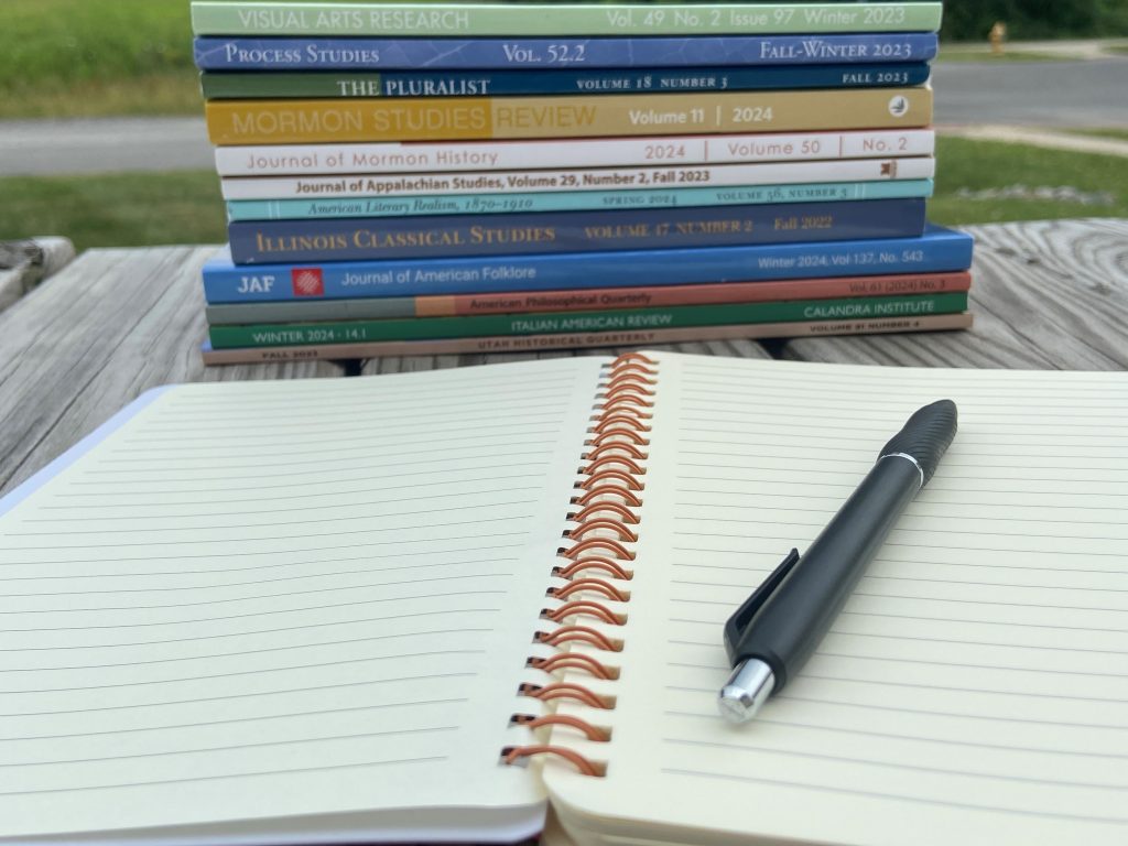 Stack of University of Illinois Press journals on a picnic table with an open notebook and pen in the foreground.
