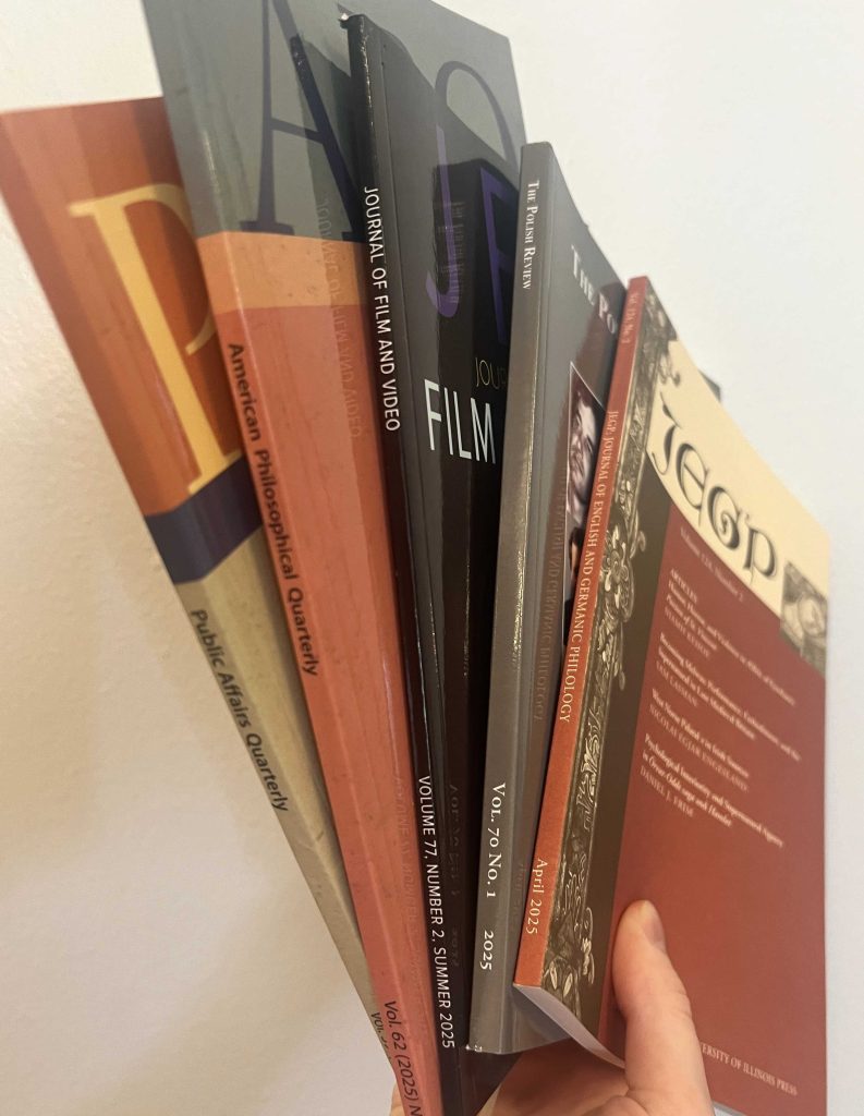 Hand holding five University of Illinois Press journals: Public Affairs Quarterly, American Philosophical Quarterly, Journal of Film and Video, The Polish Review, and Journal of English and Germanic Philology, all fanned out in front of a white background.