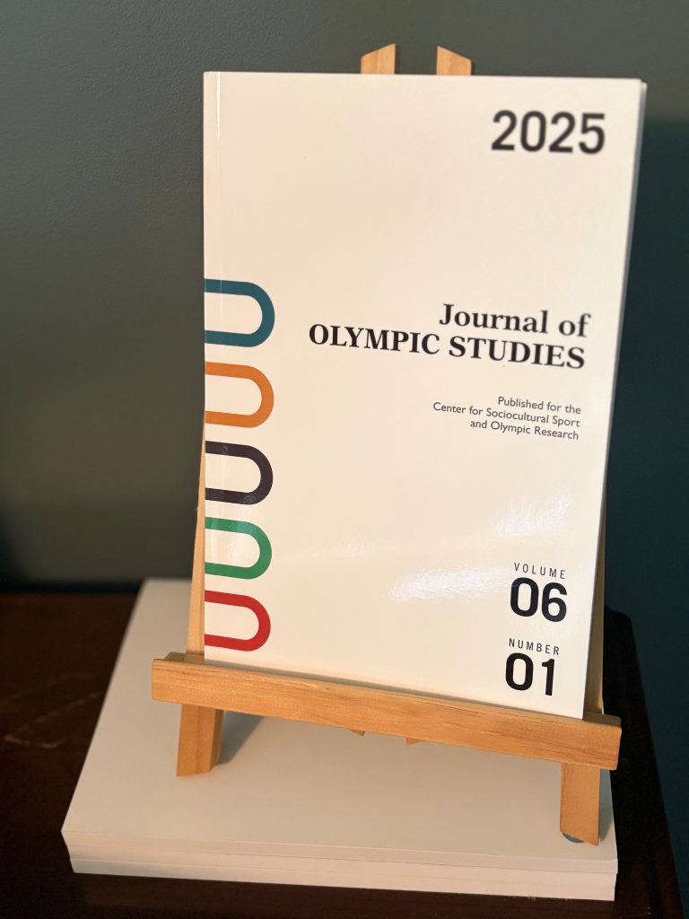 Journal of Olympic Studies Vol. 6, No. 1, on an easel resting on other issues of the journal.