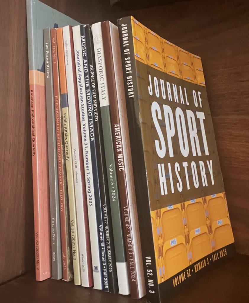 Journals on a shelf from Left to Right: American Philosophical Quarterly Vol. 62, Iss. 2, 2025; The Polish Review Vol. 70, Iss. 1, 2025; Journal of English and Germanic Philology Vol. 124, Iss. 3, July 2025; Public Affairs Quarterly Vol. 39, Iss. 2, 2025; Italian Americana Vol. 43, Iss. 1, Winter 2025; Journal of Appalachian Studies Vol. 31, Iss. 1, Spring 2025; Music and the Moving Image Vol. 18, Iss. 3, Fall 2025; Journal of Film and Video Vol. 77, Iss. 2, Summer 2025; Diasporic Italy Vol. 5, 2024 (published in 2025); American Music Vol. 42, Iss. 3, Fall 2024 (published in 2025); and Journal of Sport History, Vol. 52, Iss. 3, Fall 2025.