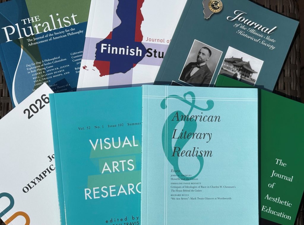 Photo of journal issues fanned out, including The Pluralist, Journal of Finnish Studies, Journal of the Illinois State Historical Society, Journal of Olympic Studies, Visual Arts Research, American Literary Realism, and The Journal of Aesthetic Education.